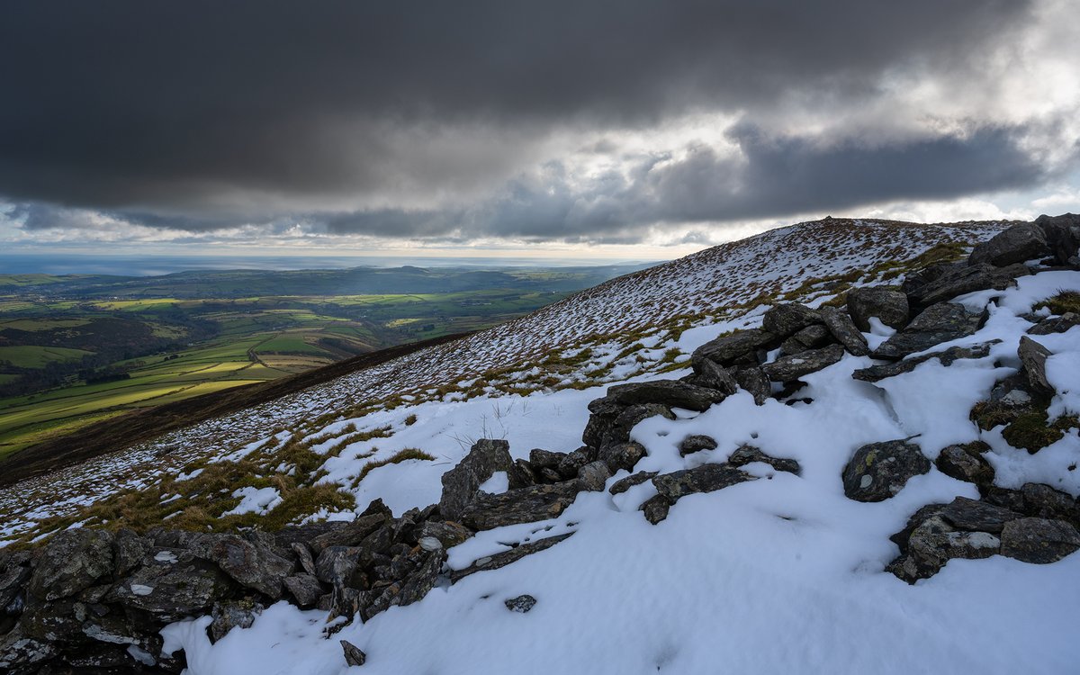 JamesBrewPhoto's tweet photo. A light dusting of snow sits on the slopes of Carraghan hill at the tail end of winter. Small fleeting windows in the thick cloud let some lovely pockets of light into the East Baldwin valley down below #iom #isleofman #landscapephotography https://t.co/wqoMUlcbhf