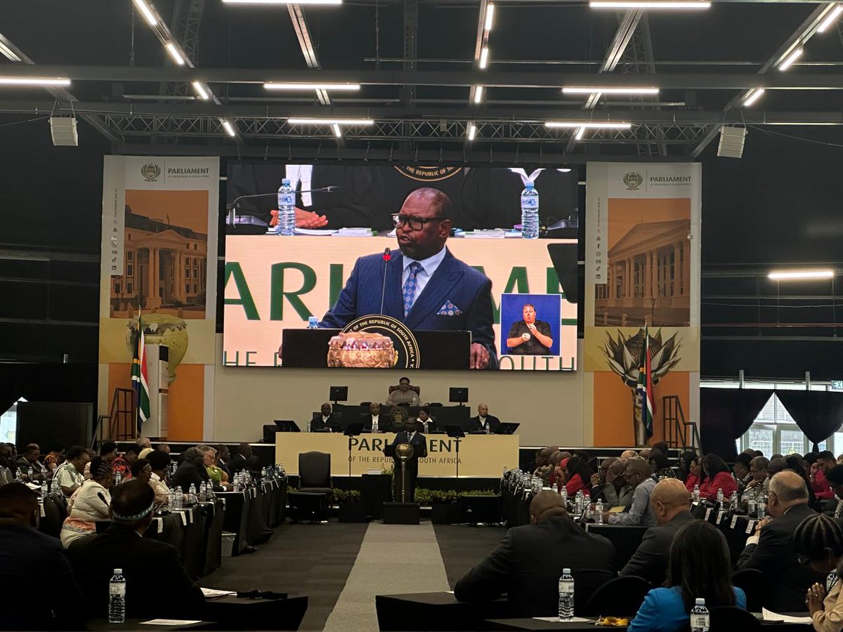 Full view of SA Parliament chamber packed with audience, large screen showing Finance Minister Enoch Godongwana speaking.