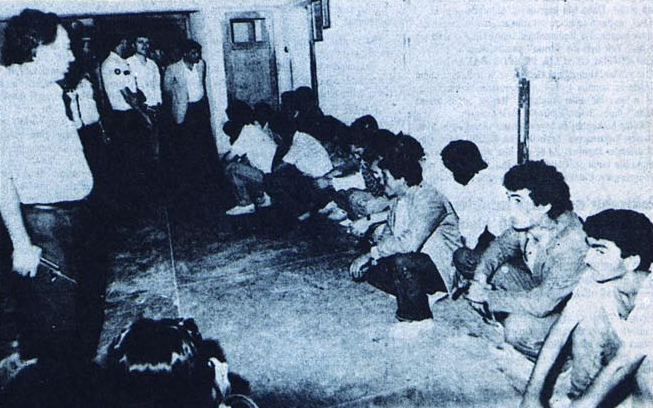 1986'da Eskişehir'de gözaltına alınan Fenerbahçeliler...
O gün şehirle savaş çıkmıştı. Önce polis gelir. Dağıtamaz. İtfaiye gelir. Olaylar üç dört saat sürer. Nihayette asker gelir. Şehirde olayların durdurulacağına dair anonslar yapılır. Bir MİT görevlisi Amigo Kemik'i bulur...