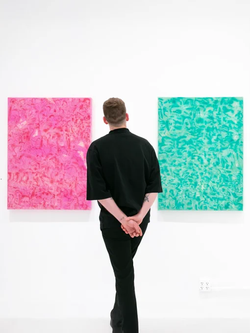 Abstract floral compositions in magenta, and green amethyst, hanging on a white gallery wall. A figure stands in front of them for scale