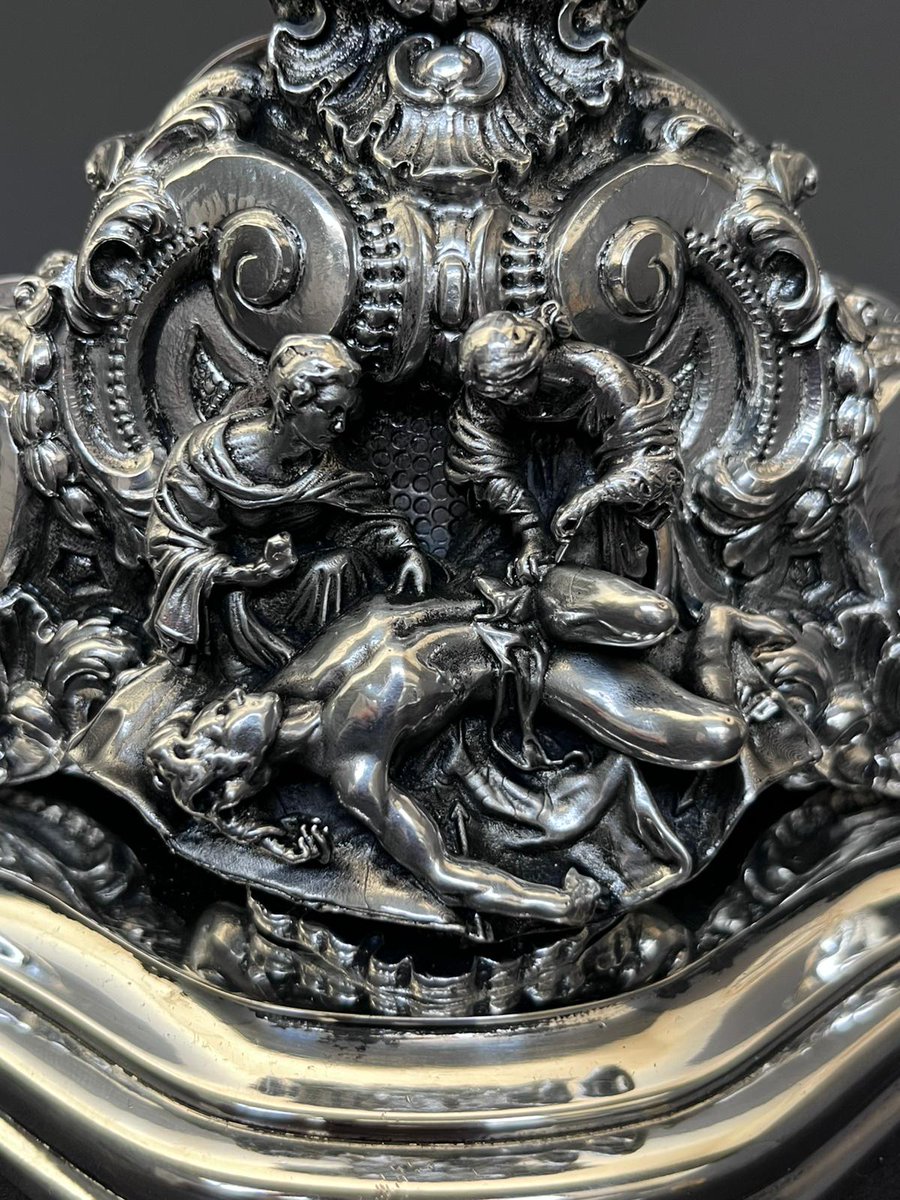 HermandadPaz's tweet photo. El relicario de San Sebastián, que abrirá el nuevo tramo de nazarenos del cortejo de Ntro. Padre Jesús de la Victoria el próximo Domingo de Ramos, obra de Ramón León, estará expuesto desde este jueves hasta el domingo 8 de marzo en la exposición 'Estrenos y Restauraciones de la Semana Santa de Sevilla 2026' del @cmisevilla .

Se trata de un Relicario portátil para una reliquia del Señor San Sebastián, con una altura total de 35 cm. Presenta una cuidada decoración de rocallas, destacando en el cuerpo central una reproducción del Santo mártir.

En la base se representa la escena de Santa Irene atendiendo las heridas de San Sebastián, aportando un notable valor iconográfico a la pieza. Los cantos bateados realzan el conjunto, mientras que el pie, de planta triangular y compuesto por molduras, ha sido diseñado para facilitar su porte durante las procesiones.

La parte posterior se encuentra decorada con una chapa calada, que conforma un delicado motivo ornamental.