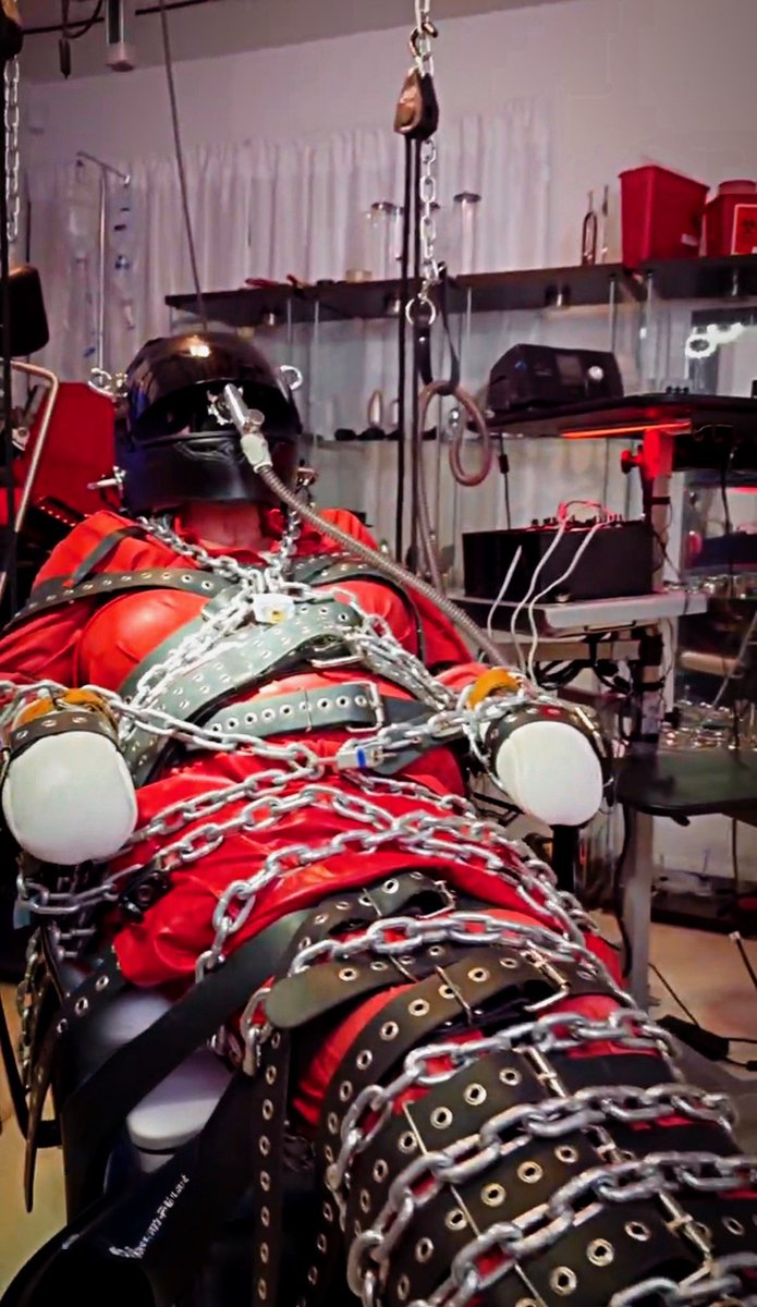 Bridget Ballard &amp; Sindy Ballard have restrained this blissfully helpless submissive just as the object they seem. Red rubber from Rubber Eva, Breast Forms, padded Bondage Mitts, customized racing helmet with anesthesia mask connected to breathing assist, leather restraints with