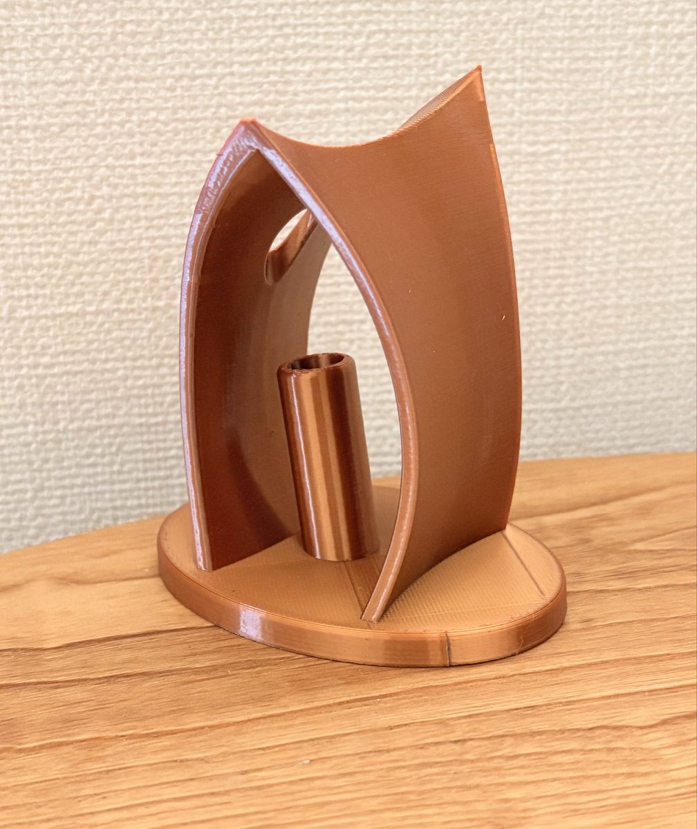 3Dプリンターでゴールドのペン立てを作っているのだけど、赤い矢印の部分が何度やっても崩れてしまう。温度設定などを、いろいろ変更してもダメだ。
それと、青い矢印の部分、底の平面部分がどうしても汚くなる。

そこで、全体を少し大きくして、底を平らにならないように設計変更した。