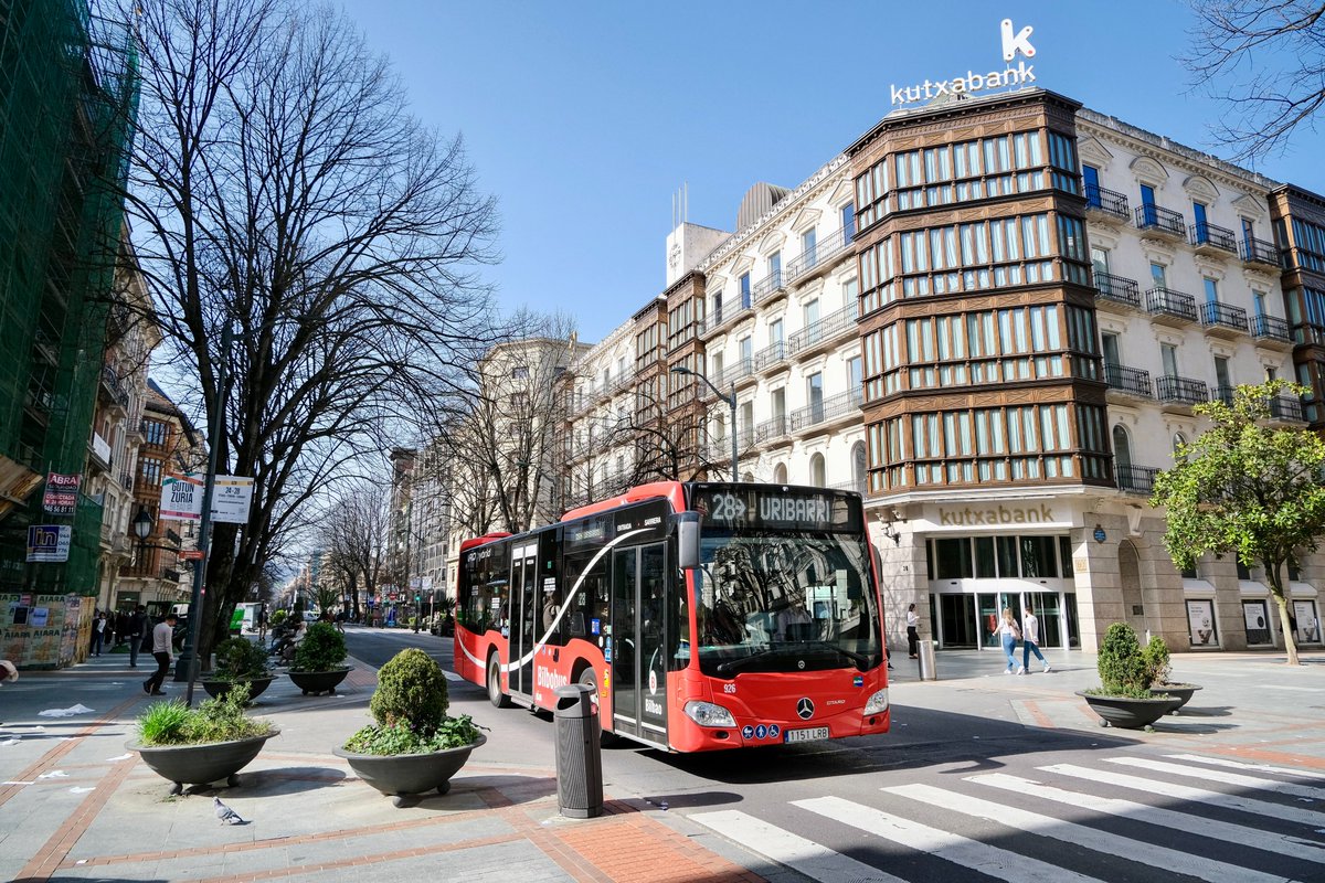 People of all ages and abilities walk, cycle, drive, and ride public transportation along the low-traffic streets of Bilbao, which are lined with buildings, trees, bike infrastructure, and prominent 30 km/h speed limit signage and road markings.