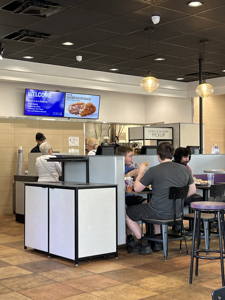 MykkiBlanco's tweet photo. Everything in America is a weird Amazon shell now. This is what’s left of the interior of a Taco Bell, a framed painting denoting a more festive past inside a grayscale soulless box. DAMN https://t.co/yWqCH7lDs5