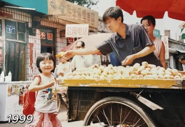 manyapan's tweet photo. Just a warm story amid all the heavy news.

In 1999, 3-year-old Wang from Jiaozuo in Henan was on a family trip to Taiyuan in Shanxi with her parents when her dad snapped a pic of her in front of a fruit stall on Yijing Street. The old photo became a treasured childhood memory for Wang, who, now 30 years old and an avid social media user, decided to return to that very same street while visiting Taiyuan during this year’s Spring Festival.

Turns out the fruit seller from 1999 was still there, at the very same spot. His wooden fruit cart has been converted into a modern shop, the street has widened, and the public phone booth in the back has been replaced by 5G mobile phone shops. Fruit stall owner Yang Guoping (杨国平) initially hardly recognized himself in the photo. At the time, he was just starting out as a young single guy. Now he’s a married dad of two adult kids. He says he still remembers that moment 27 years ago — because it was rare for people to take photos in those days.

Wang’s social media posts about the reunion are now going viral, and Yang, who’s been in the fruit business for 30 years, is profiting from it. People are coming to the shop to check it out, and he’s put the 1999–2026 reunion photo on display in his shop window.

The photo’s virality has a lot to do with nostalgia, and with how quickly China’s urban landscape is changing, so it feels rare to see some things remain the same. Beyond the elements of this story that are uniquely Chinese, I feel the universal value is that a single snapshot moment can impact our lives decades down the road, a sweet moment can be remembered forever, and strangers on the street can quietly become an important part of our personal history. So we’d better remember that small moments matter, and to be kind to each other. And especially to 3-year-olds, because they may look like babies today, but are growing into the big influencers of tomorrow.