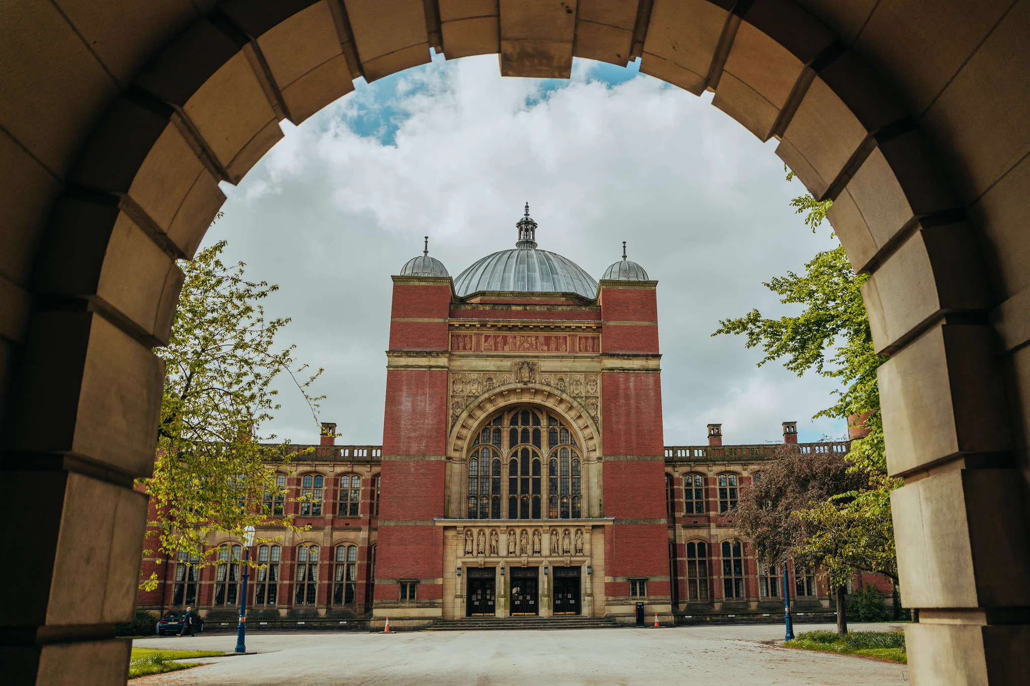 Exterior view of the historic red brick Aston Webb building, framed by a stone archway 