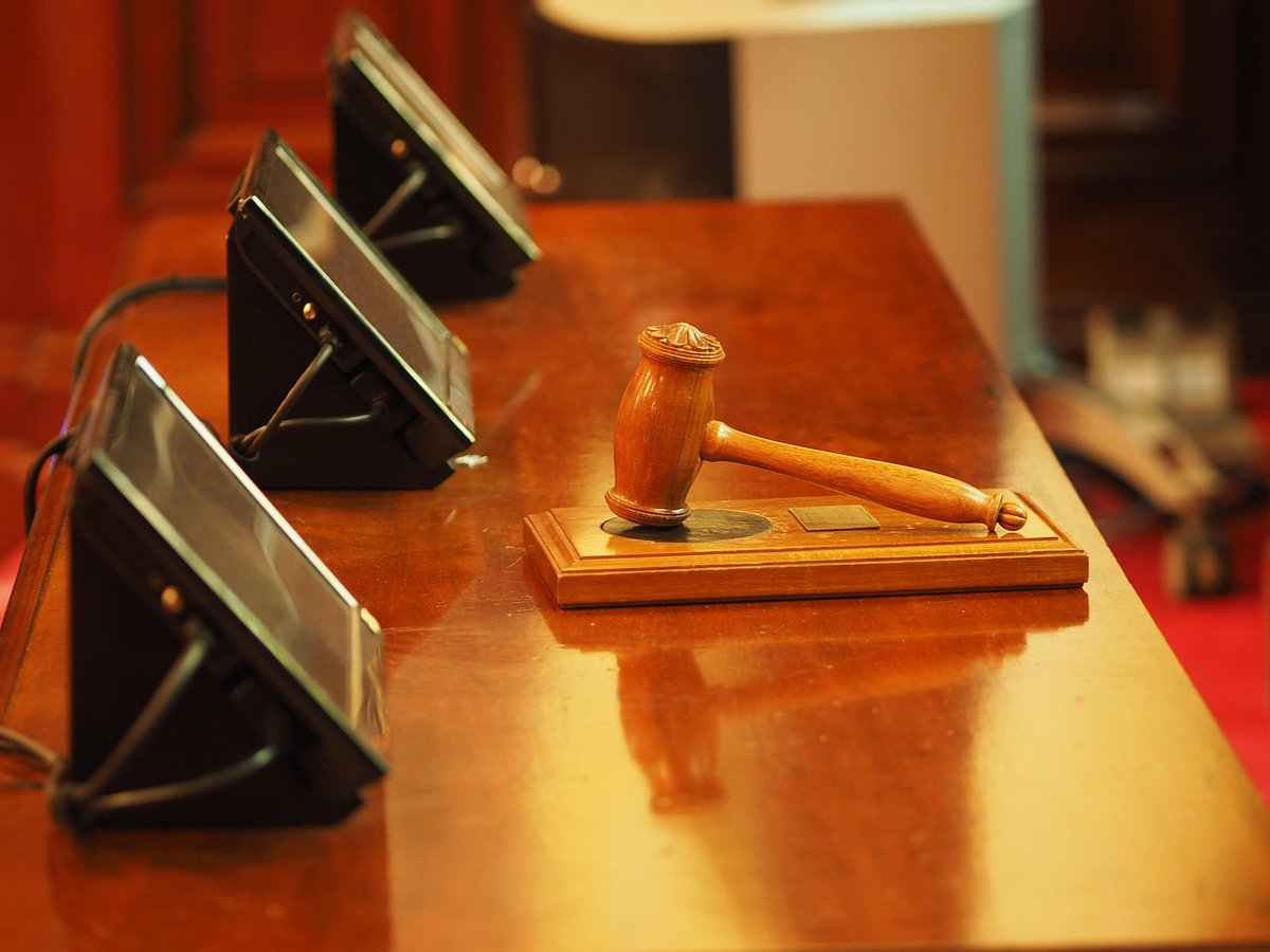 Wooden gavel on sound block atop polished courtroom desk with black monitors nearby on glossy table.
