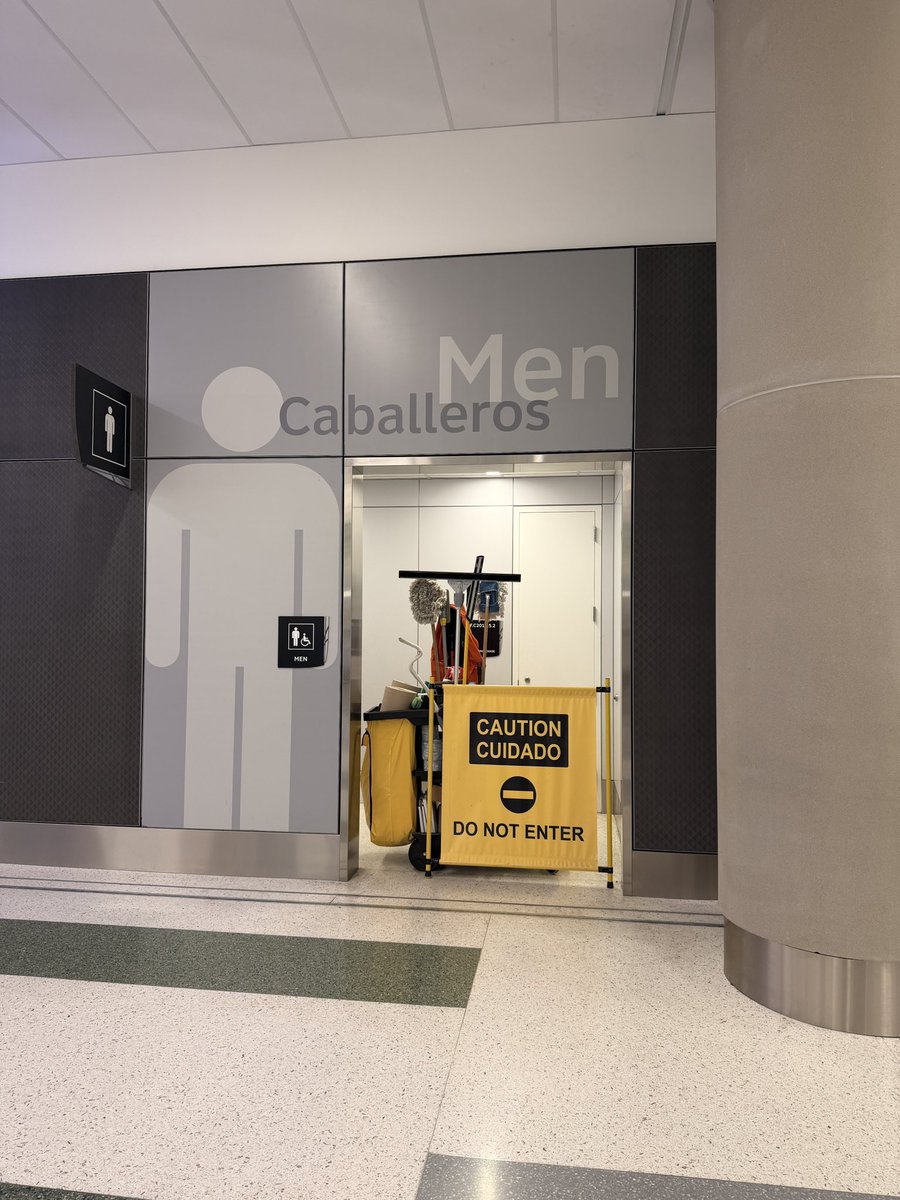 retaliashun's tweet photo. Once again, @iah, the one men’s restroom in this area is closed, not due to being out of order, but because they can’t hire male janitors.   The lady “cleaning” has been rearranging her cart the last 10 minutes, not cleaning https://t.co/VhwTnJJ2G1