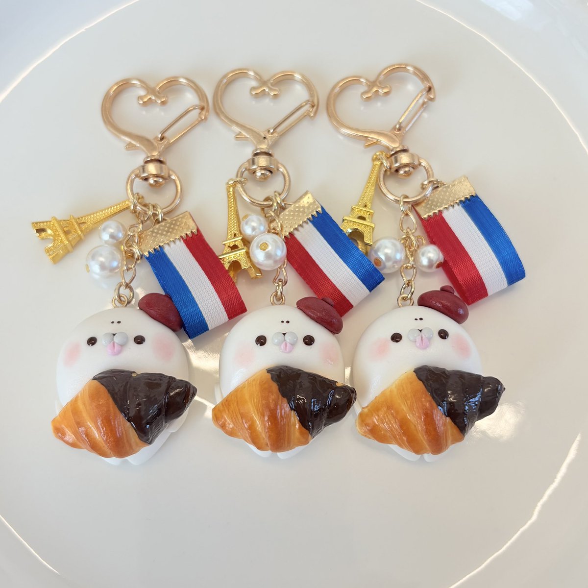 EClaycraft's tweet photo. 2027のヨコハマハンドメイドマルシェに出たいから（早すぎやろw）
育児の合間で早速作品づくり♡

デザフェスで完売したあざらしちゃんシリーズの中で人気だったフレンチ！
新しくトリコロールのリボンを付けて更に🇫🇷感満載に･:*+.\(( °ω° ))/.:+

あざとい癒し、🦑がですか？🦭🇫🇷🥐

#ハンドメイド https://t.co/LSikINK6XQ
