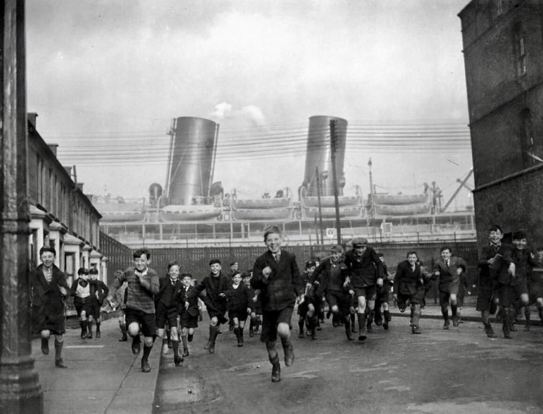 The_East_End's tweet image. Jan 1932 - children pour out of their school in Drew Street, Silvertown, with the liner ‘Rajputana’ in the background. This image has been used in many a TV programme about the East End of London... the-east-end.co.uk #eastend #schooldays