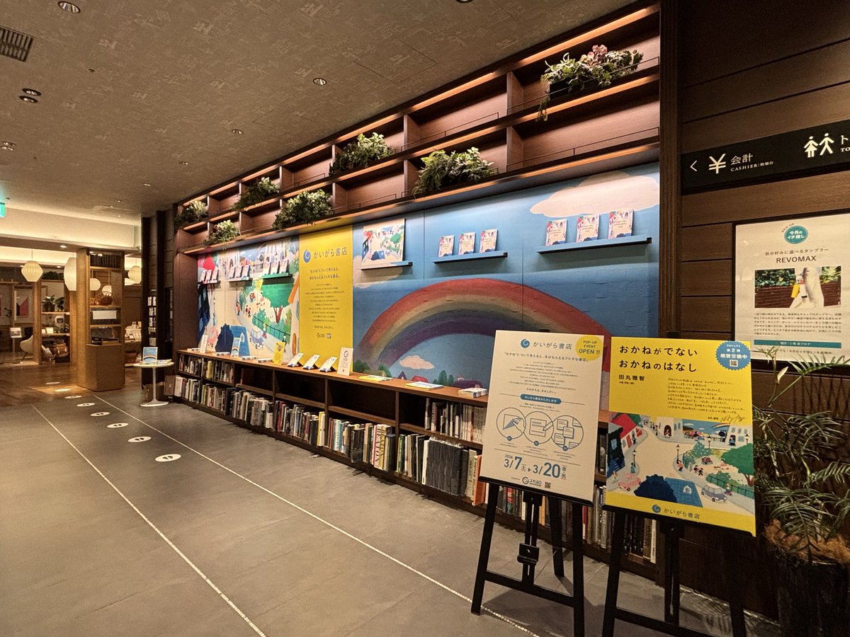 kaigarabooks's tweet photo. 明日オープンのかいがら書店ですが、会場のセッティングが完了しました

ショートショートの作中に出てくる「虹みがき」を模した大きな虹の絵が目印です🌈
今はくすんでいますが、参加者の皆さまにシールを剥がしていただくと、綺麗な虹が徐々に完成していきます。

向かって左側の絵は、大桃洋祐さんに手がけていただいたショートショートのカバー絵です。
こちらには剥がしたシールの裏に書かれたお金に関する問いかけへの回答を貼り付けていきます💰
他のみんなの答えも見てみよう！
詳細はコチラ▶https://t.co/zKoJt7wkyJ