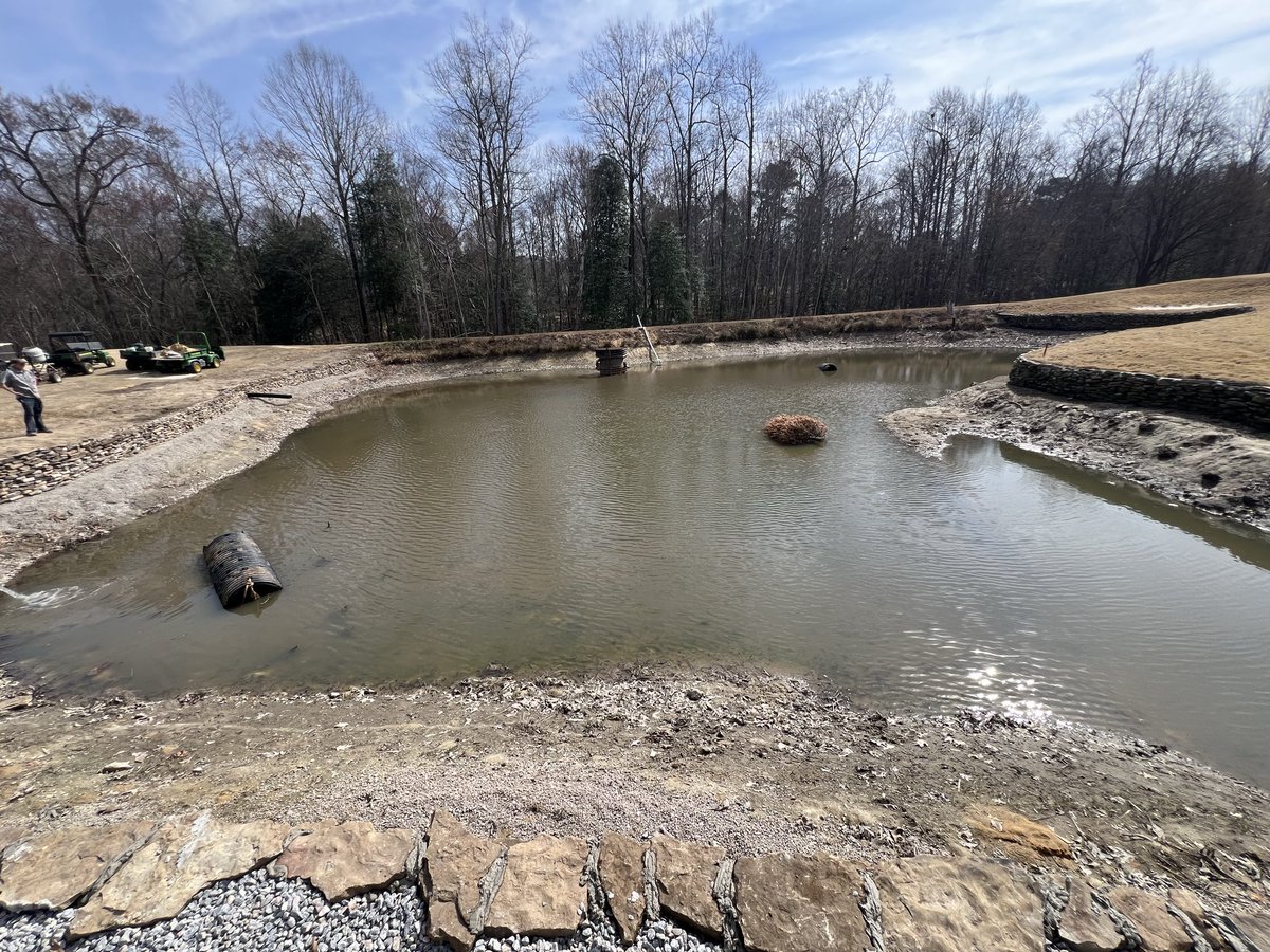 riverridgegolf's tweet photo. Last step on the inside of dry stack wall on 16 pond. Cementing the top layer. Notice the reused pipe and Christmas tree for fish cover. Stocking fish in a month. 17 pallets, 34 tons rock, one by one. Installed during winter 2024-25 and 2025-2026. https://t.co/BqcDXMBxVf