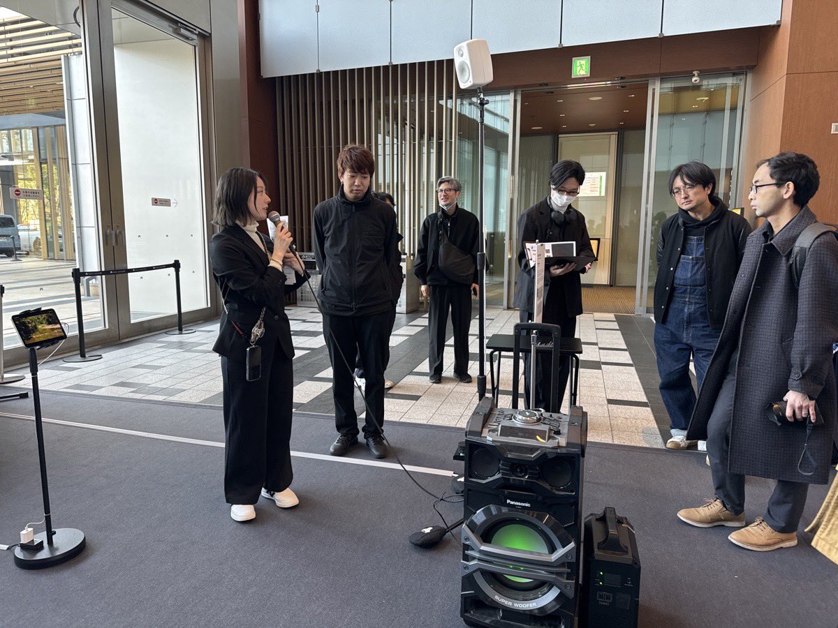 nobi's tweet photo. #ARTxJAPANCONTEXT

「ART X JAPAN CONTEXT.」最終作品発表・展示会
各作品紹介【後編】

以下、各作品の背景説明である。

* **EXP2FLOOR×WOMB：「LOOOPs on the FLOOOR」**
* DJと観客の関係性をクラブイベントで実験し、成熟したスタイルに対し、より能動的な関わり方を模索するプロジェクトである。
* 日常体験（音楽を聴きながら街歩き、ドライブ選曲など）をゲームや楽器として実装。翌日、新宿の王城ビルで実際のクラブイベントを実施予定である。
* **ドライブVJ作品**: 車でのドライブ映像をVJ（ビデオジョッキー）に使用。東京（新宿、六本木）だけでなく世界各地（アイスランド、ロードアイランド、ニューヨーク）の映像を収録し、プレイヤーが道を変えたり、左右に旋回したり、都市を裏側や高所から見たりできるインタラクティブな要素を持つ。
* **足音を使った楽器作品**: 音楽を聴いてステップを踏む現象を利用。観客の足音をリアルタイムで加工し、テクノミュージック風にする楽器であり、DJがテクノミュージックに観客の足音をオーバーレイする実験を翌日のイベントで実施予定である。

* **池田翔×Lada：「おとがたりの列島」**
* フィールドレコーディングした複数の音素材を、単一空間に5つ配置するプロジェクトである。
* 128個のスピーカーが連なる黒いバー状の特殊スピーカーを使用し、特定のポイントに立った時のみ音がはっきり聞こえる仕組み。ラダプロダクションと電通ライの技術協力により制作され、空間内の人数や位置情報によって音の位置や残響などのパラメーターがリアルタイムで変化する。
* 美術館の絵画展示のように、複数の音作品を同一空間で同時に体験できることを目指し、従来の音の展示における「一つの空間に一つの音」という課題を解決する試みである。

* **石田康平×レゾナック・ホールディングス：「住居に夢幻を埋蔵する」**
* 建築、デジタルテクノロジー、VR（仮想現実）を専門とする背景から制作された作品である。
* 壁の奥にリバーブ（残響効果）を配置することで、そこにない空間を感じさせるバーチャリティ（仮想性）を創出。複数の壁を立て、それぞれ異なる音を流すことで、一つの空間に多様な空間性を生み出す。
* 仏教の「三世」（過去世、現在世、未来世）の世界観をテーマに、時間を水の流れで表現。茶室や数寄屋の考え方をリファレンスとし、市松模様をベースにしたデザインである。
* **紙袋箔と時間の表現**: 日本建築における箔が光を反射するのに対し、「時間を反射するもの」として紙袋を使用。「紙袋箔」は、見ることで当時の時間が想起され、自分の時間も重なるモチーフとして機能する。小田原学祭の茶室にある「暦張り」（カレンダーを貼った仕上げ）をレファレンスに、デジタルのビットの白黒イメージとモザイクを組み合わせた壁面デザインである。
* **着せ替え建具のコンセプトと社会実装**: 455モジュールの組み合わせだけで壁が作れ、簡単に分解・組み立て可能な「着せ替え建具」の設計。鴨長明の組み立て式家から着想を得て、裏地の壁（気温・音響反射制御）と表地の壁（表現）の二層構造を持つ。災害時の避難所でのプライバシー保護や、オフィス設計における外部性の取り込みへの応用可能性をレゾナック・ホールディングスとのコラボレーションで検討中である。
* 虎ノ門で2週間程度の展示を予定しており（紹介制）、奈良で展示していた作品を改めて出展する可能性もある。壁パネル226枚（実際は約210枚）を手作業で制作するプロセスも重要視されている。

@Plaud_Japan で録音して生成した取材データはこちら:

https://t.co/lPVkVD5065