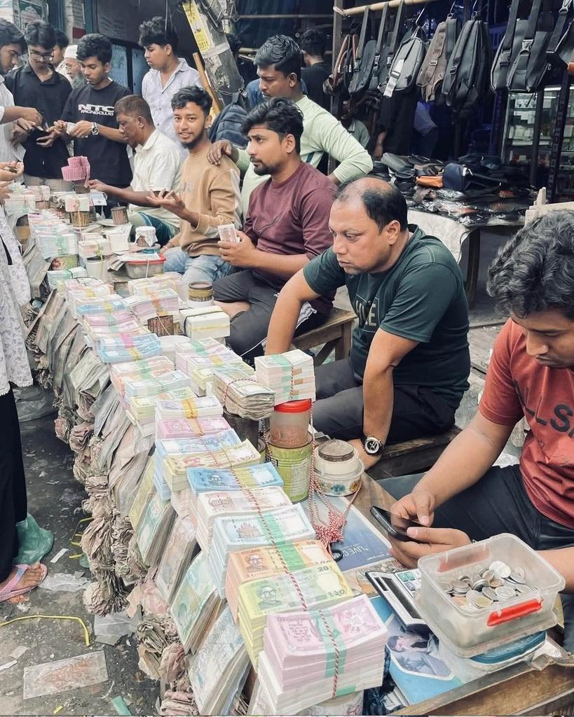 ব্যাংকে নতুন টাকা পাওয়া দুষ্কর, অথচ রাস্তার পাশে নতুন টাকার অভাব নেই।
যে টাকা আসার কথা ব্যাংকের মাধ্যমে সরাসরি জনগণের হাতে, সেটাই কিভাবে যেন আগে চলে যায় রাস্তার পাশের বিক্রেতাদের কাছে!

সাধারণ মানুষ ব্যাংকে ঘুরে নতুন টাকা পায় না, কিন্তু একটু বেশি টাকা দিলেই রাস্তার পাশে সহজেই