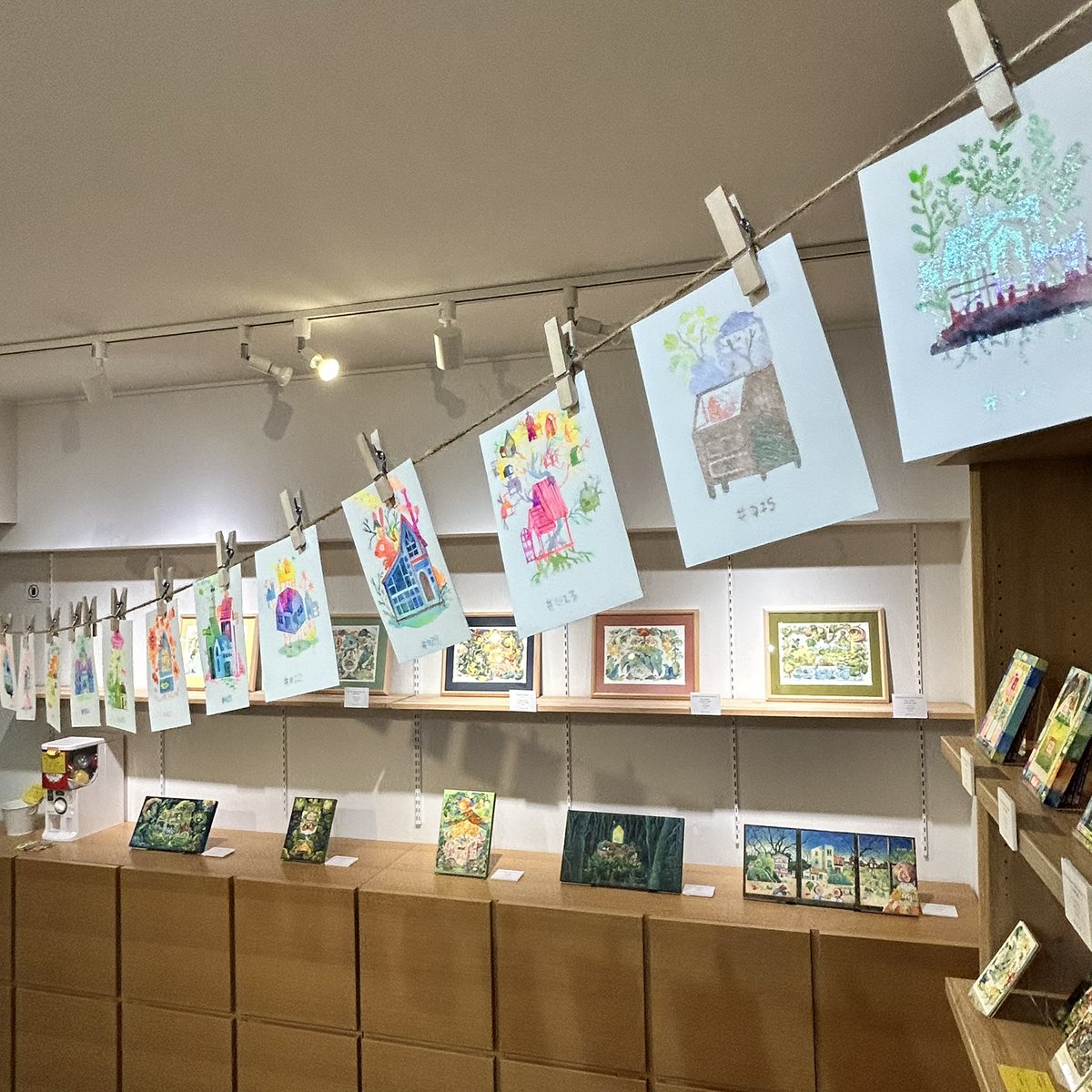 ガーランドフラッグ、全て手描きです

装丁夜話の中に洗濯バサミでアンバーさんの絵をガーランドのように吊り下げました
かつてない珍しい光景！
可愛い「箱庭ハウス」が吊り下げられています

Amber Ma「いちじく少年　箱庭の無限」
2026.3.20金／21土／22日、27金／28土／29日
<a href="/amberwonderland/">Amber Ainsworth</a>