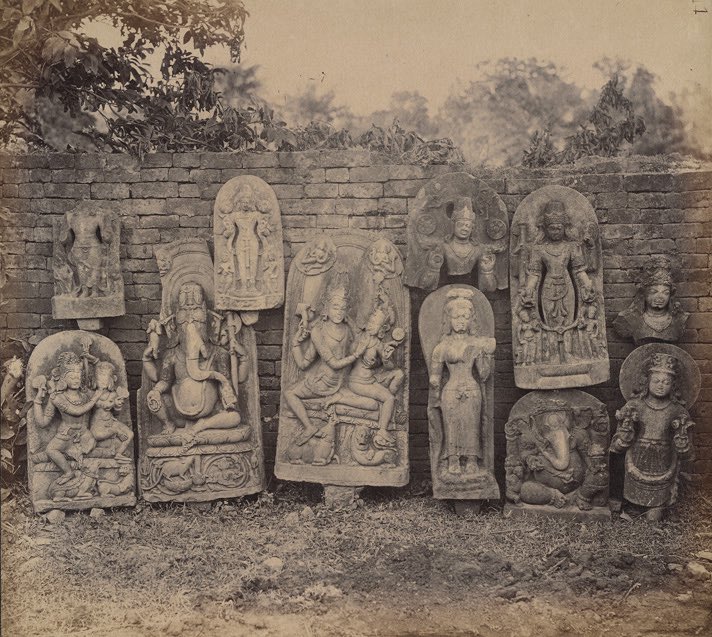 A group of sculptures arranged against a wall, of Ganesha, Uma-Maheshwara, Vishnu, and the Adityas at Bodh Gaya, 1880–81.