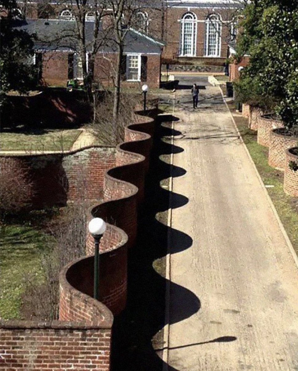 archeohistories's tweet photo. In England 🏴󠁧󠁢󠁥󠁮󠁧󠁿🇬🇧 you sometimes see these “wavy” brick fences. And curious as it may seem, this shape uses FEWER bricks than a straight wall. A straight wall needs at least two layers of bricks to make is sturdy, but the wavy wall is fine thanks to the arch support provided by the waves... 

These are called crinkle-crankle walls. They appear whimsical at first, like they were designed for aesthetics, but their origins are actually engineering. A straight brick wall that is only one brick thick is structurally weak — it can be pushed over or can collapse under small lateral forces. To make a straight wall stable, you usually need two courses of bricks side by side, which doubles material usage. But when you introduce a repeated serpentine curve, the wall gains strength because every bend acts like a buttress. The load paths distribute sideways pressure through the sinusoidal shape, stabilizing the wall without additional mass.

This design became especially common in parts of England where landowners wanted long boundary walls but wanted to reduce cost. Over a long distance, one course of bricks snaked back and forth could save thousands of bricks compared to a straight double-width equivalent. Garden estates adopted the pattern in the 18th and 19th centuries, especially in East Anglia. The geometry also had horticultural advantages — microclimates formed in the concave pockets which made them popular as fruit walls. Warmth collected on the south-facing curves, protecting apples and pears.

Modern viewers think they are decorative first, but historically the decoration was a side effect of cost efficiency and structural logic.

Thomas Jefferson even built crinkle-crankle walls at Monticello in the United States after seeing the concept in England. 

© Reddit

#archaeohistories
