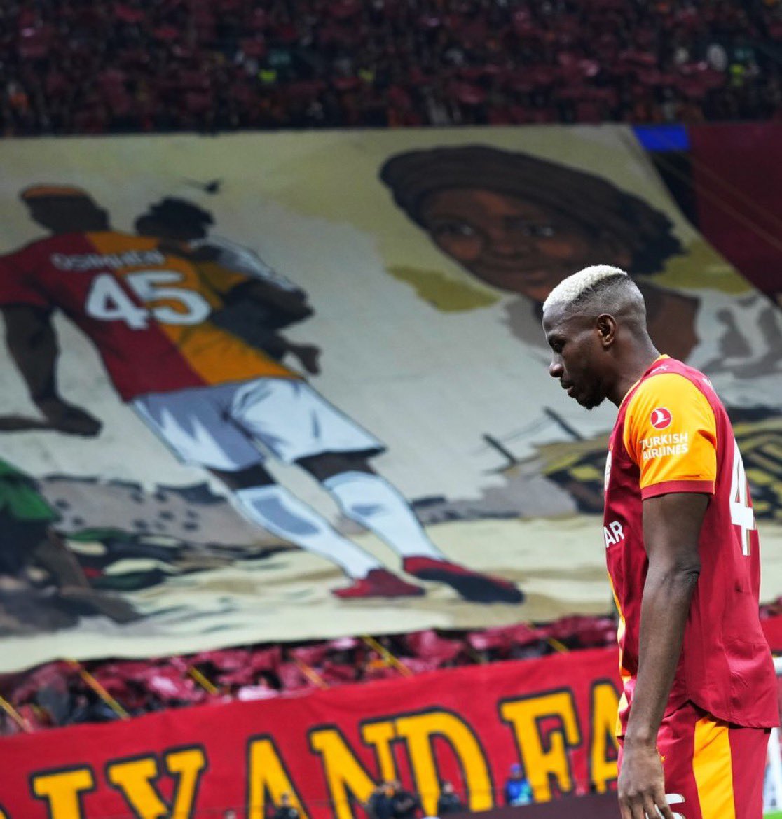 OJogoEscrito's tweet photo. Hoje a torcida do Galatasaray mostrou para o mundo o motivo de Victor Osimhen se sentir tão bem no clube.

A torcida do clube turco fez um mosaico em homenagem ao atacante, com uma imagem da Mãe que ele perdeu aos 3 anos de idade.

Toda vez que ele marca em algum jogo grande ou faz algum golaço todo mundo se pergunta o porque um jogador de nível tão alto, que teria espaço nos maiores clubes do mundo, está jogando na Turquia no seu auge técnico e físico.

Osimhen saiu do Napoli, clube que ganhou destaque mundial, cercado de polêmicas e questões, a sua relação com a torcida e diretoria era nada boa, ele chegou a ser ridicularizado pelo perfil do próprio clube no TikTok por um pênalti desperdiçado.

Isso tudo fez o Nigeriano buscar um caminho que o valorize como jogador e pessoa, com o Napoli complicando negociações com vários clubes como Chelsea e Al Hilal, o Galatasaray surgiu como solução, primeiro foi emprestado e em junho de 2025 foi comprado em definitivo por 75 milhões de Euros, um recorde histórico de transferência na Turquia.

Lá ele vem recebendo carinho e respeito que não ganhou na Itália, mesmo sendo o melhor jogador do país, agora ele é tratado como ídolo nacional e vem correspondendo dentro de campo, liderando tecnicamente o clube turco em busca de uma campanha histórica na Champions League.