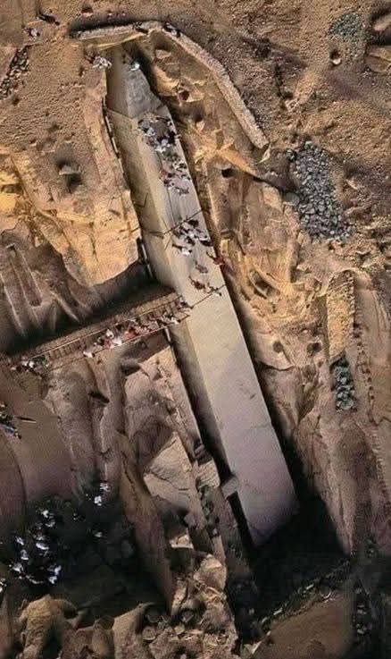 The Colossal Unfinished Obelisk 🏜️🗿

Seen from above, a massive stone monolith lies partially carved within a granite quarry, still attached to the bedrock. Visitors standing along its edges reveal its astonishing scale. This unfinished obelisk offers rare insight into ancient