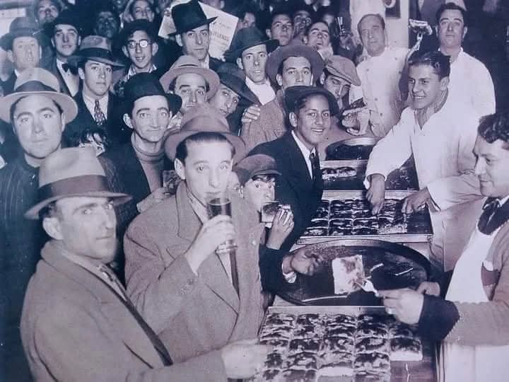 PIZZA EN LA BOCA, comiéndola a la vieja usanza, de pie y con un vino Moscato. Las pizzas no siempre fueron redondas. Año: 1929.