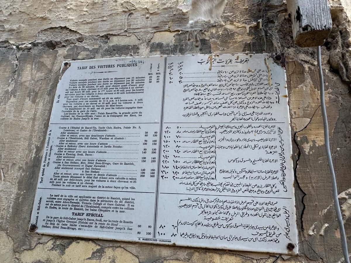 Alexandria_egy1's tweet photo. 🎞️ تخيل إن اللوحة دي مازالت لحد النهارده في شارع فؤاد بالإسكندرية.

اللافتة دي تعتبر وثيقة تاريخية نادرة، لكنها ماخدتش حقها من الشهرة، وهي لوحة تعريفة عربات ركوب الحنطور مكتوبة بالعربي والفرنساوي، ومقسومة لثلاث أجزاء:
•تعريفة داخل المدينة
•تعريفة خصوصي من وإلى خارج المدينة
•تعريفة مناطق الرمل وسيدي جابر

الأجمل إنك تقدر من خلالها تعرف حدود مدينة الإسكندرية زمان، واللي كانت محددة كده:
“سراي رأس التين – باب القباري الكبير – الشانزليزيه – وابور المياه – تلول الحضرة لحد البحر”.

وتلول الحضرة المقصود بيها التلال اللي كانت موجودة قبل تسويتها وبناء المقابر ومستشفى كوتسيكا اليوناني ومعهد فاروق الأول للصحة العامة.

والغريب إن أماكن إحنا شايفينها دلوقتي وسط البلد كانت وقتها خارج المدينة، زي:
الكلوب البحري – إسبيتالية الجيش الإنجليزي – سراي نمرة 3 – لمبروزو – كازينو الإبراهيمية.

يعني مناطق زي جناكليس أو شارع كنيسة الأرمن كانت تعتبر وقتها صحراء وبعيدة عن العمران، وحتى الإبراهيمية نفسها من حوالي 150 سنة ما كانتش داخل النطاق العمراني للإسكندرية.

المعلومة الأهم إن اللافتة دي ليها حوالي 5 نسخ، ولسه موجودة لحد الآن، ويفضل نقل واحدة منها على الأقل إلى المتحف القومي بالتنسيق بين المحافظة والآثار لأنها قطعة تاريخية حقيقية.

كبر الصورة واقرأ التفاصيل…
هتكتشف قد إيه شكل الإسكندرية اتغير.

- mina zaki