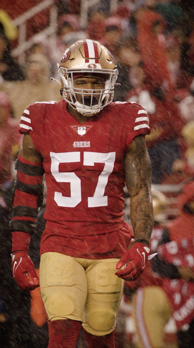 San Francisco 49ers football player wearing jersey number 57 in the red and gold uniform with helmet, standing on the field during what appears to be rainy conditions.