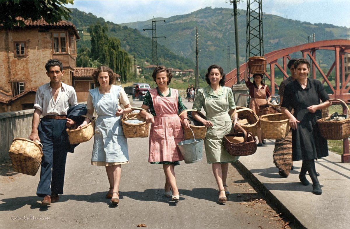 1947. Varias mujeres y un hombre volviendo del mercado con cestos al brazo. El Entrego, San Martín del Rey Aurelio, Asturias. Al fondo, el puente de hierro en arco sobre el Nalón.  Una foto hipnótica que rebosa optimismo.