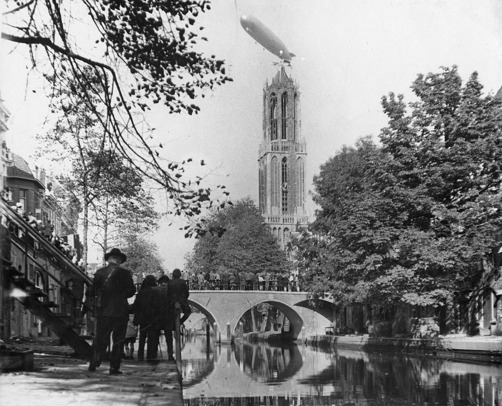 ZowasUtrecht's tweet photo. Oudegracht. Het Duitse luchtschip Graf Zeppelin boven de Domtoren in 1929. Het publiek op werf en Hamburgerbrug kijkt toe. De Hamburgerbrug is (in verbasterde vorm) vernoemd naar het voormalige middeleeuwse stadskasteel Rodenburg dat in de 12e eeuw hier vlakbij stond #diedomdaar https://t.co/N9HTM2j55w