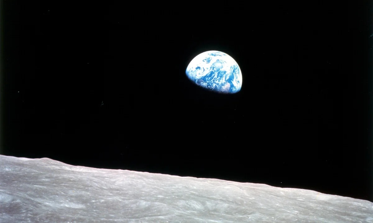 Earthrise, captured on December 24, 1968, during NASA's Apollo 8 mission. This image shows our planet rising above the lunar horizon, with the gray, desolate surface of the Moon in the foreground and the half-illuminated blue-and-white Earth hanging in the black void of space. It