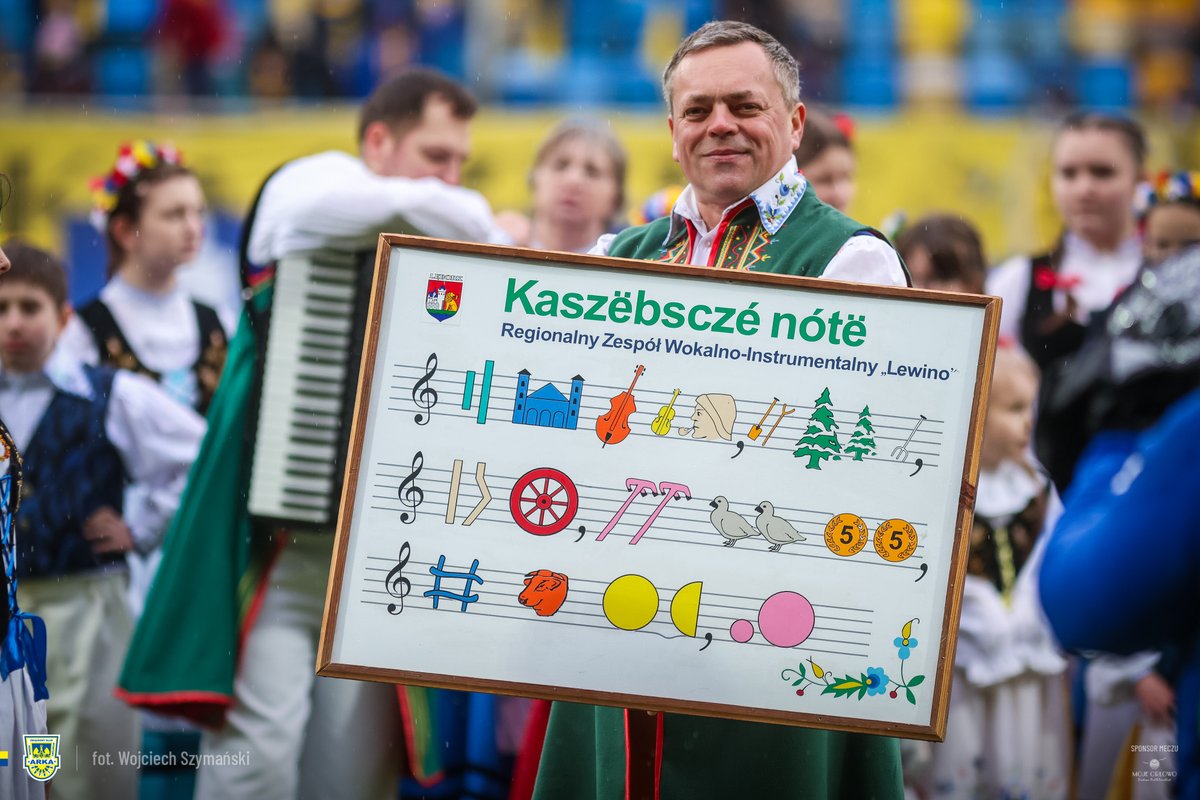 ArkaGdyniaSA's tweet photo. ℹ️ Za nami dzień meczowy #ARKWID, w którym Arka Gdynia po raz kolejny aktywnie celebrowała Dzień Jedności Kaszubów. Niedzielnemu spotkaniu towarzyszyła wyjątkowa, kaszubska oprawa. ⚫️🟡

🎵 Hymn kaszubski wykonała Weronika Korthals wraz z chórem La Via Voice,
🎤  Rotę Arki Gdynia odśpiewał Tomasz Fopke,
🎶 Wokół stadionu przygrywała Kapela Kaszubska z Kostkowa, 
🎲 Na placu Janusza Kupcewicza odbywały się rozgrywki w tradycyjną grę - buczkę,
🥨 Na stoisku Koła Gospodyń Wiejskich z Lubkowa serwowano lokalne przysmaki i wypieki,
🧵Rękodzieło kaszubskie prezentowały twórczynie ludowe Magdalena Lelwic i Aleksandra Zadrożna,
🎁 Gadżety i akcesoria kaszubskie dostępne były na stanowisku Farwa,
🌿 Przed stadionem stoisko wystawił tabaczarz Henryk Lessnau,
🏁 Na murawie zaprezentowano najdłuższą, mierzącą 95 metrów, flagę kaszubską, którą wynieśli: Kaszubski Zespół Pieśni i Tańca "Levino" z Lęborka, Zespół Folklorystyczny "Nadolanie", Akademia Piłkarska Cassubian oraz Zespół Szkół Katolickich w Gdyni.

Dziękujemy, że byliście tego dnia z nami #naStadionie! 🫵

Wokół meczu: 📝 https://t.co/bZW7NzOSJS