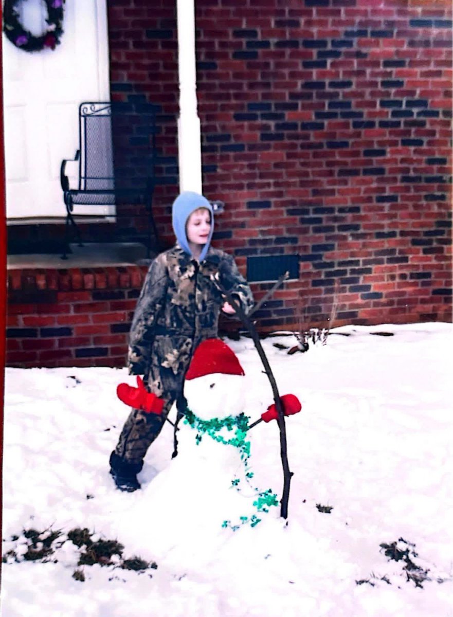 AutismOnFire's tweet photo. @NWSGSP Here’s a photo of me at age 8 during this winter storm. I remember it because it was right after St. Patrick’s Day 2004 (hence the green garland on the snowman). https://t.co/wUeW27TEBK