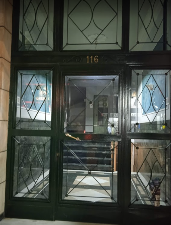 Εδώ βλέπουμε μία πόρτα παλιάς πολυκατοικίας ανάμεσα σε δύο τσαντιρομάγαζα και έναν κάδο γεμάτο σκουπίδια, ο οποίος συμπληρώνει το παρακμιακό ντεκόρ. Στις άλλες φωτογραφίες έχουμε την είσοδο της πολυκατοικίας, η οποία όπως βλέπετε είναι αρχοντικότατη, με πανάκριβα μάρμαρα, με