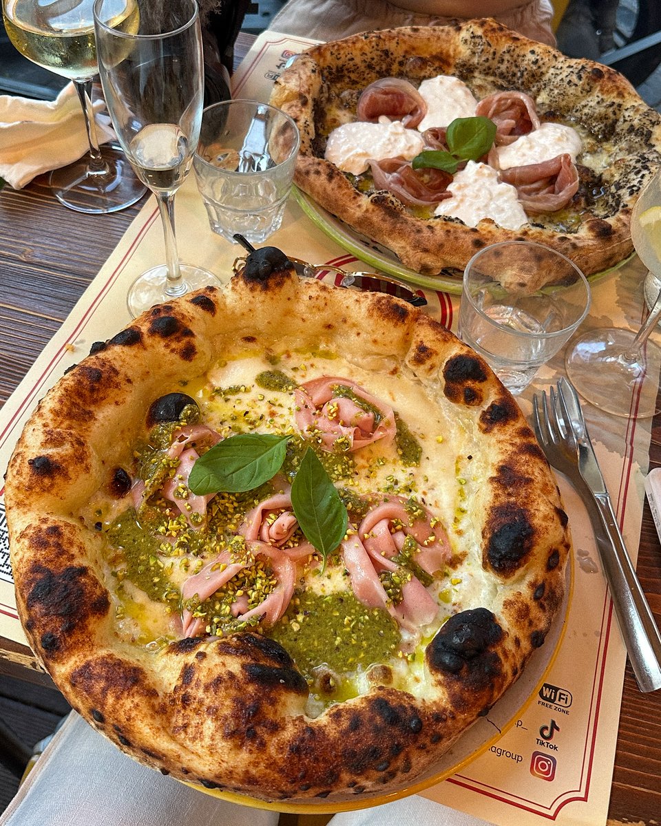 A meticulously crafted, handmade pizza, perfectly presented. Pesto, Burrata cheese, and a glass of wine—it's heaven! Every bite tells a story of flavor. Do you like pizza too?