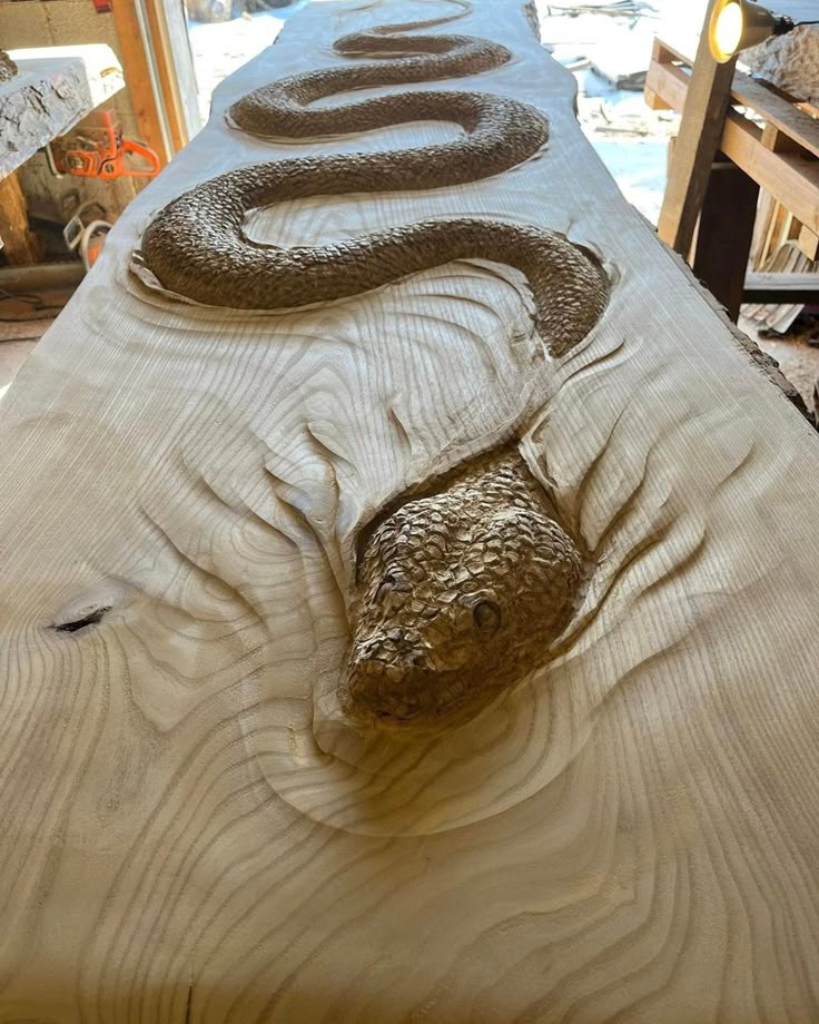A detailed wood sculpture of a snake emerging from a plank of wood, created by artist Scott Dow.