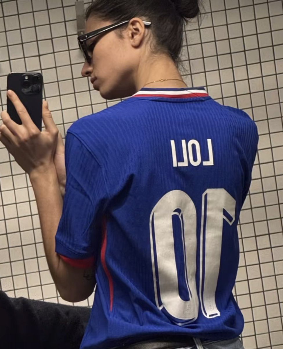 updaterosalia's tweet photo. ROSALÍA was wearing this T-shirt from her girlfriend Loli Bahia underneath the coat she was wearing today at the airport. https://t.co/qM1FGT0Cy5