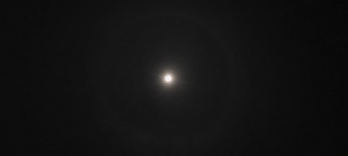 इस तस्वीर में चंद्रमा के चारों ओर एक चंद्र प्रभामंडल (जिसे 22-डिग्री प्रभामंडल के रूप में भी जाना जाता है) दिखाई दे रहा है।