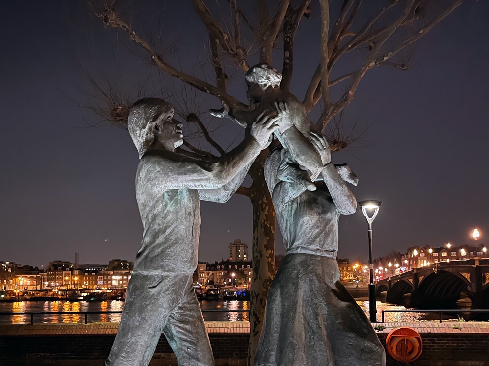 ArmadilloLED's tweet photo. Subtle uplighting brings John Ravera’s bronze "In Town" to life at Riverside Plaza - right by the southern end of Battersea Bridge. Parents joyfully lifting their child toward the sky, a tender symbol of family love, elegantly glowing against the Thames and city skyline by night. https://t.co/tyXYCpXJ12