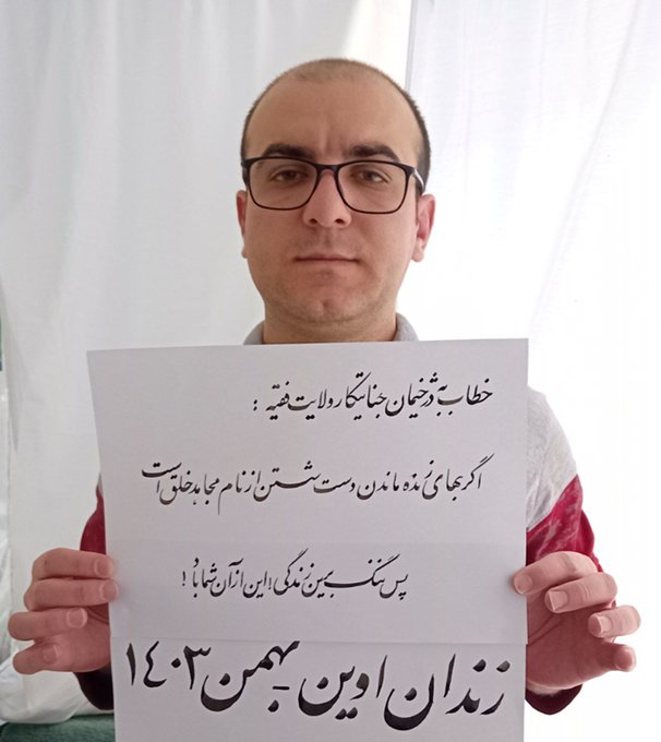 en_simayazadi's tweet photo. A picture of PMOI member Pouya Ghobdi in prison shows him holding a sign addressing the regime’s executioners: “If the price of staying alive is renouncing the name of a PMOI member, then shame on such a life.” 
Pouya and his fellow PMOI member, Babak Alipour, were executed on March 31 at dawn.