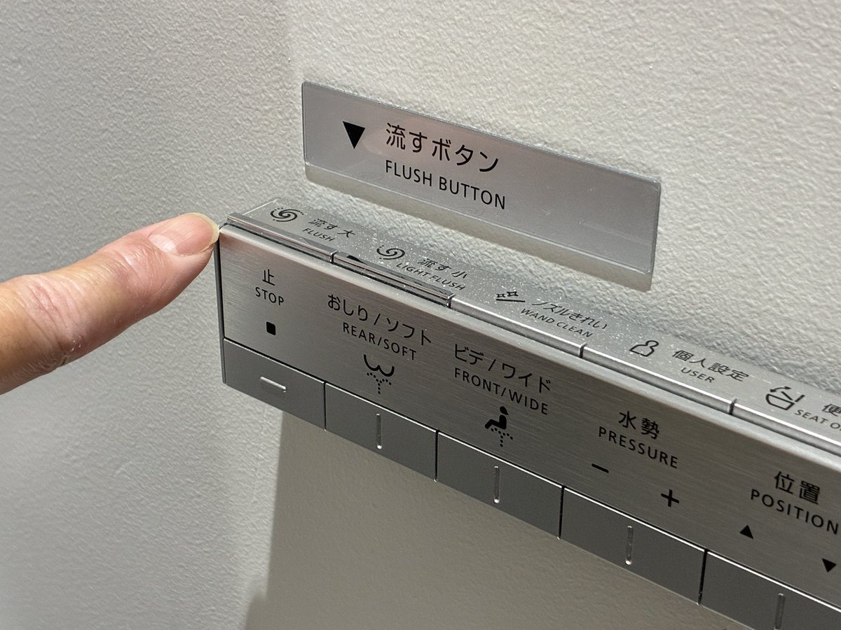 トイレの「流す」ボタンの写真。操作者の目線からだとボタンが目立たないため、目立たせるための追加表示が取り付けられている。使いやすさは改善したが、プロダクトデザインとしてかなり無理がある。#todaysuxd #UX