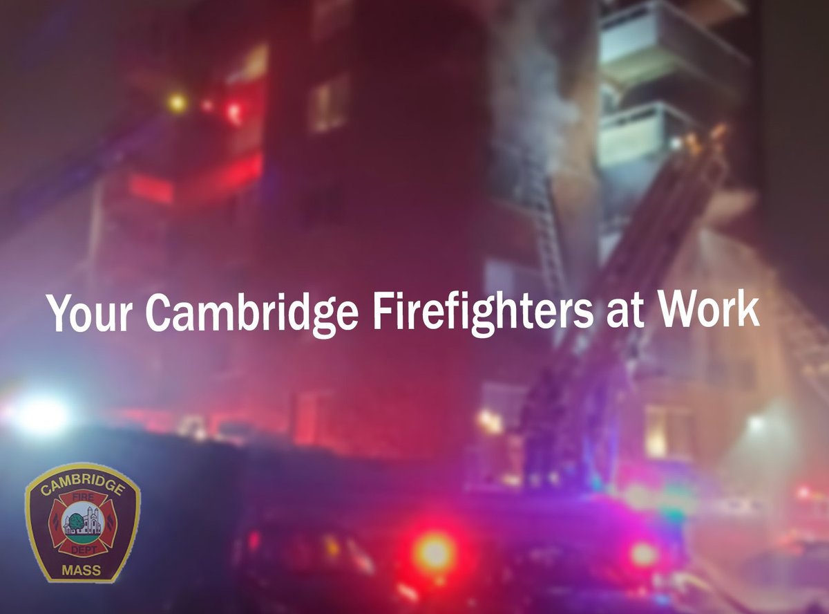 A nighttime fire scene showing firefighters actively working at a multi-story building in Cambridge, Massachusetts. There are firetruck ladders extended to upper floors with visible smoke. Bright emergency lights illuminate the scene. The image includes the text "Your Cambridge Firefighters at Work" and features the Cambridge Fire Department emblem.