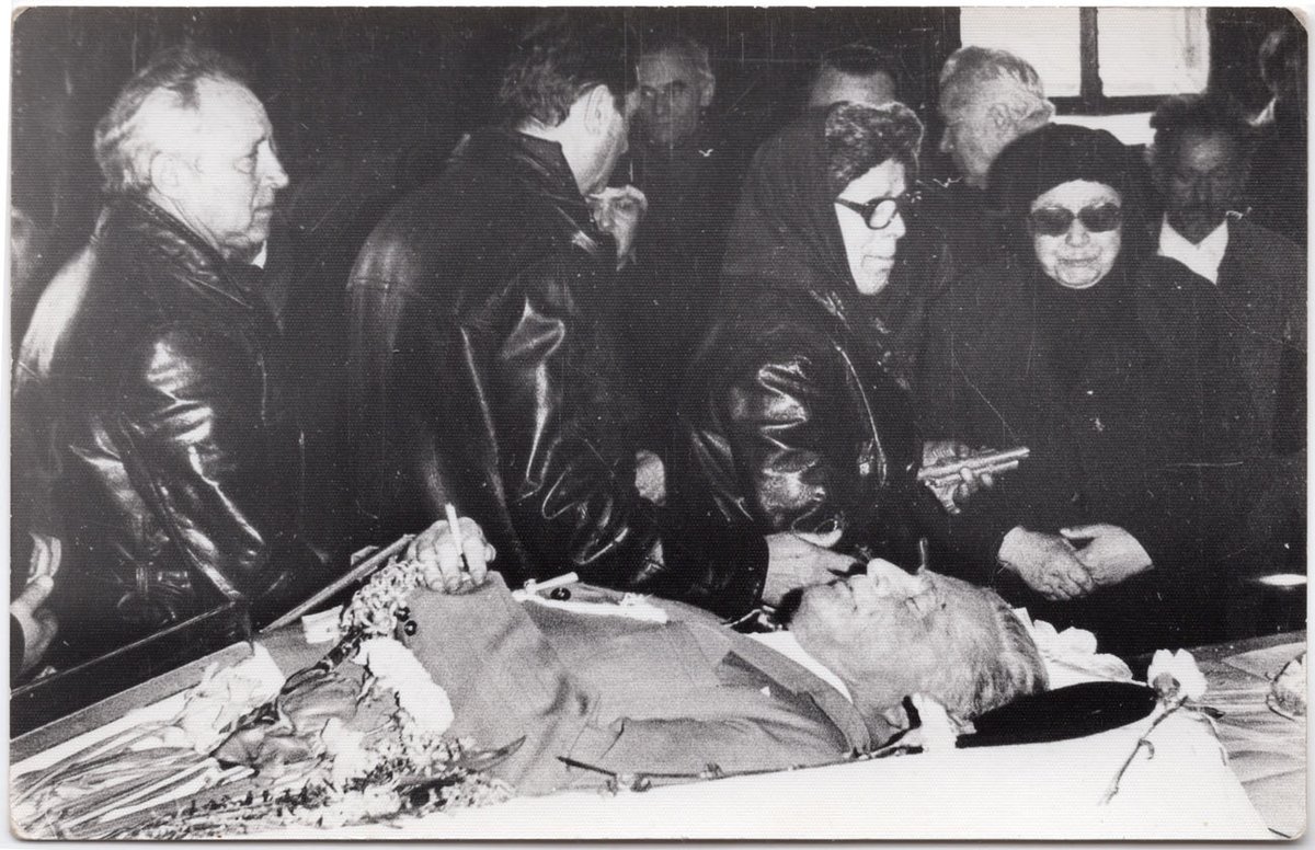 ルーマニアの死後写真（ポストモーテム）。年代不詳。

亡くなった男性のまわりを、黒い服を着た多くの弔問客が訪れている。よく見ると遺体の指の間にはタバコが挟まれており、おそらくタバコ好きだった故人へと贈られた最後の一服なのだろう。