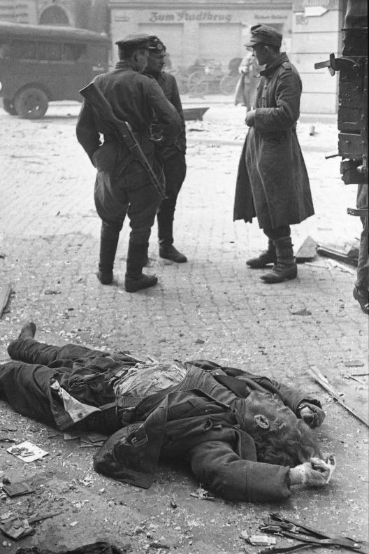 ShoahUkraine's tweet photo. Spring 1945. Soviet soldiers speak with a German prisoner on the street of the captured town of Forst.

A dead German soldier is in the foreground. https://t.co/18lXOw40rt