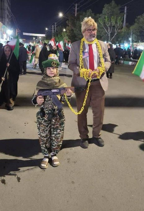 Ihsannasim's tweet photo. "ایک ایرانی بچی نے اپنے والد کو منایا کہ وہ ٹرمپ بن جائیں! وہ خود فوجی بنی ہے، اور والد صاحب جو ٹرمپ کے حلیے میں ہیں، ہتھکڑیوں میں جکڑے ہوئے ہیں۔ بہادر قوم کے بہادر بچوں کی یہی پہچان ہے۔" https://t.co/DLpofiw2so