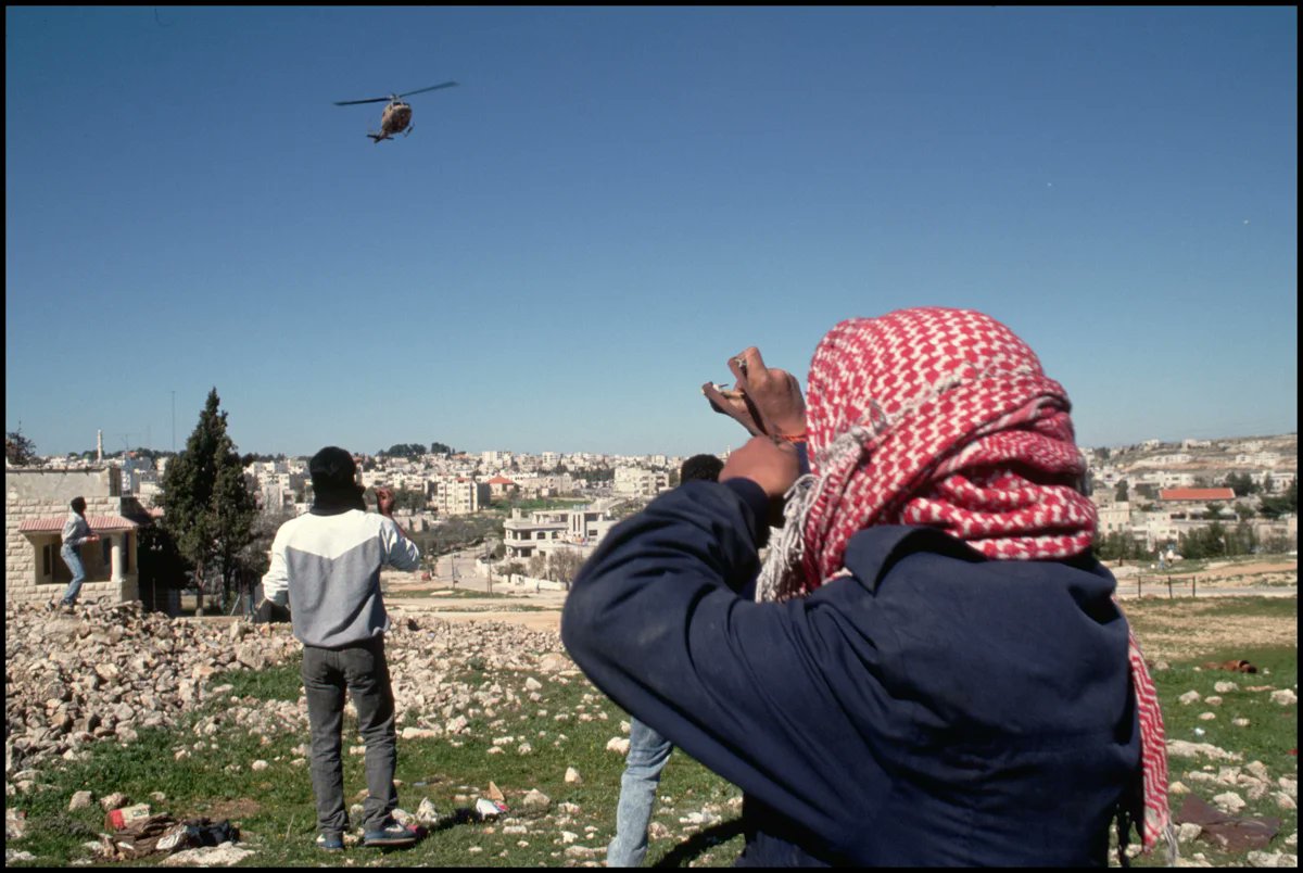 eyeonaxis's tweet image. Palestinians throw rocks at a helicopter of the occupying Israeli military forces. West Bank, Palestine, 1988 | Peter Turnley