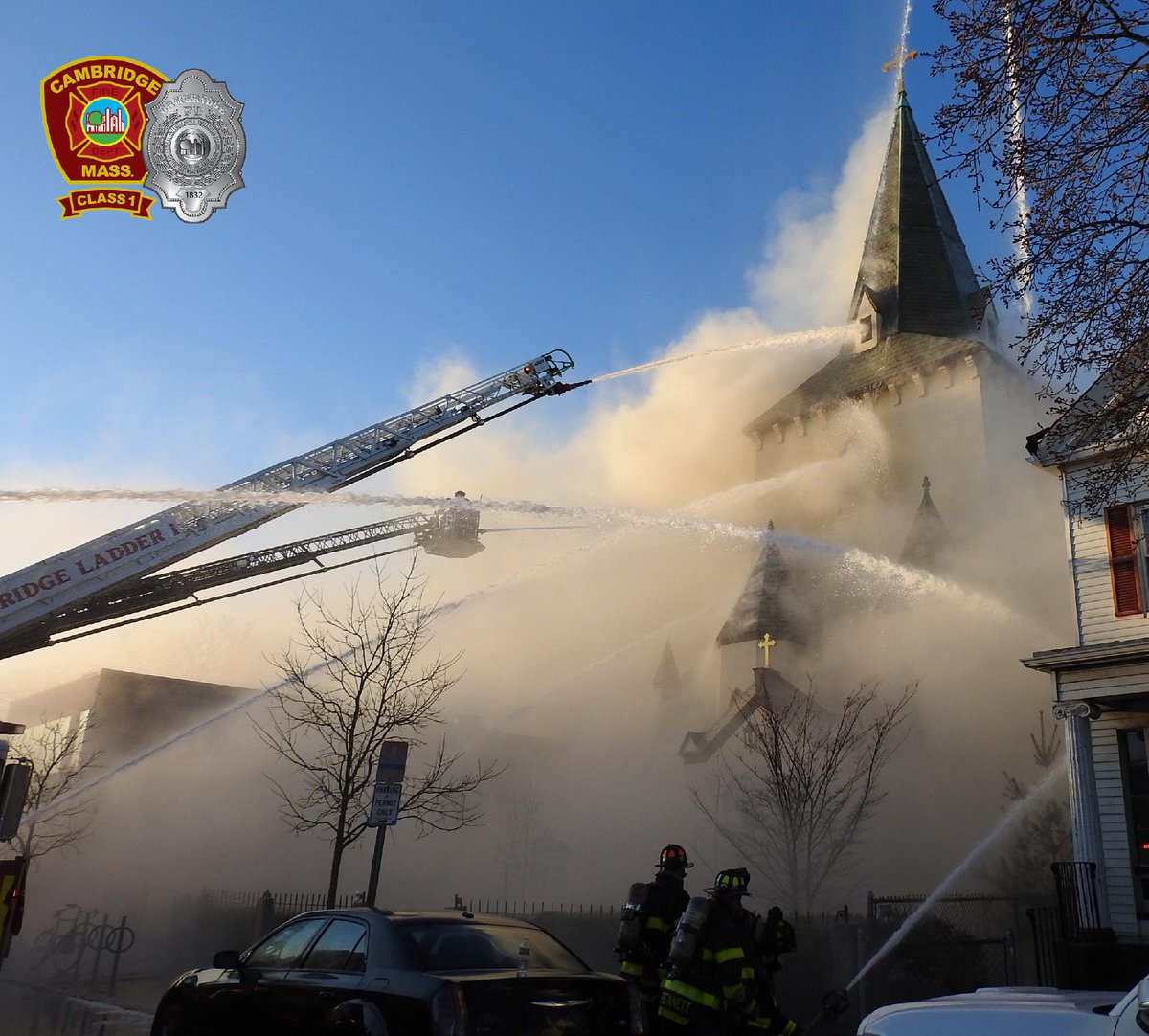 Firefighters are battling a fire at a church engulfed in smoke, using multiple hoses and ladder trucks. The Cambridge Fire Department logo is visible in the top left corner.