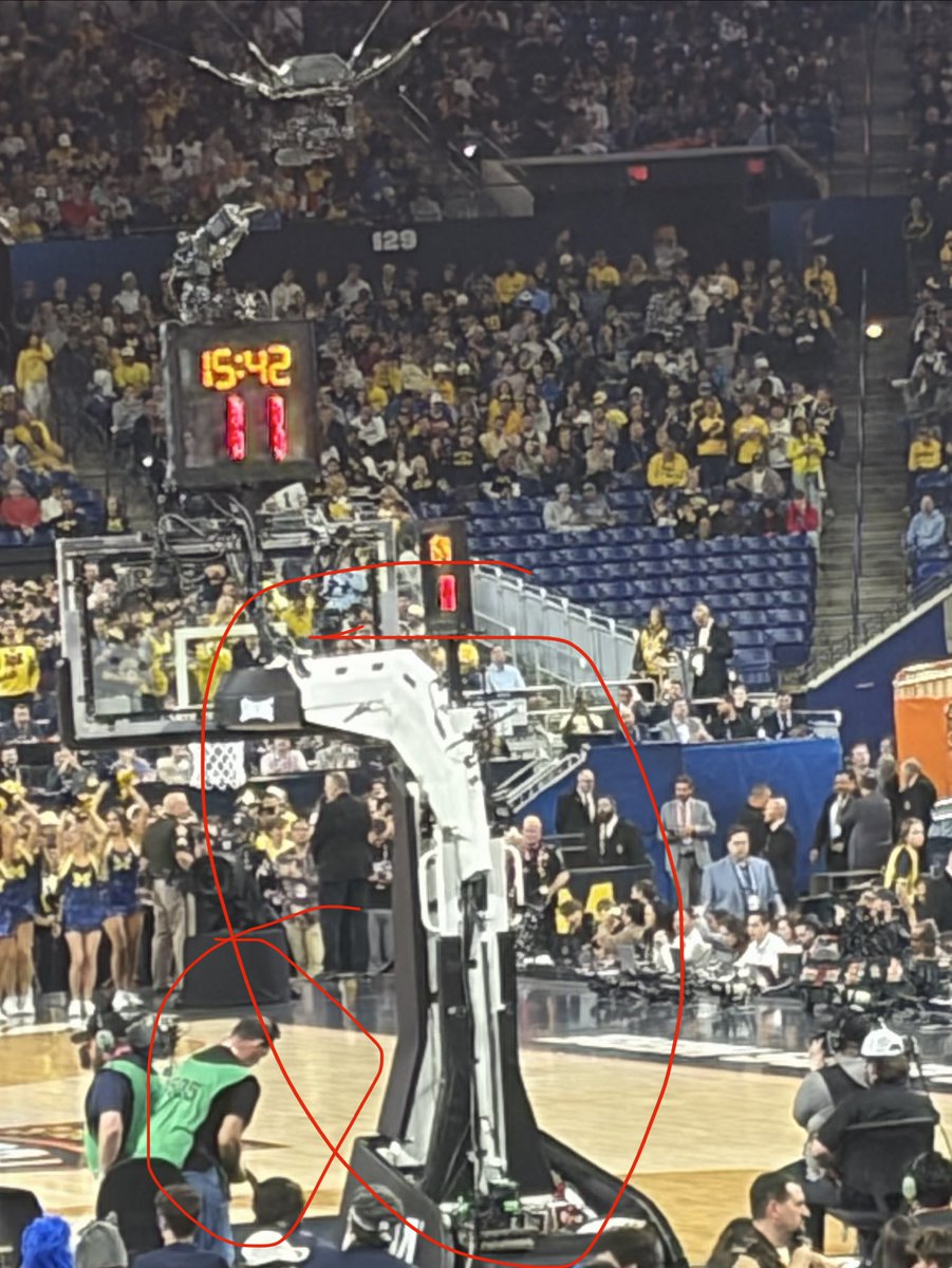 RIGGEDFORVEGAS's tweet photo. I sat behind the basket for the national championship  to prove that there is some artificial force impacting the outcome of certain shots going in vs bouncing out. In the first half I obtained a preponderance of evidence of just that. Look at this gentleman circled here, he would consistently be toying with the backside of the basket during the entirety of the first half. (Michigan missed every single 3 point attempt in the first half on this side of the court pictured). Secondly look at this drone floating around, at first glance it doesn’t look like much as it is a standard drone used for optics to get better close up views/angles of fans and players, but one odd thing I noticed during the game was the synchronicity of the timing of the drone flying by vs when shots were attempted/results of those said shots. It wasn’t every time but there was a significant (70%+) higher number of made baskets when the drone was en route behind the basket of the  side of the where the team had possession vs when the drone was not on that side of the court. Yes it sounds crazy, but after seeing the UConn Illinois game, and the Nebraska Vanderbilt game you’d have to be an utter fool to not at the bare minimum question it.