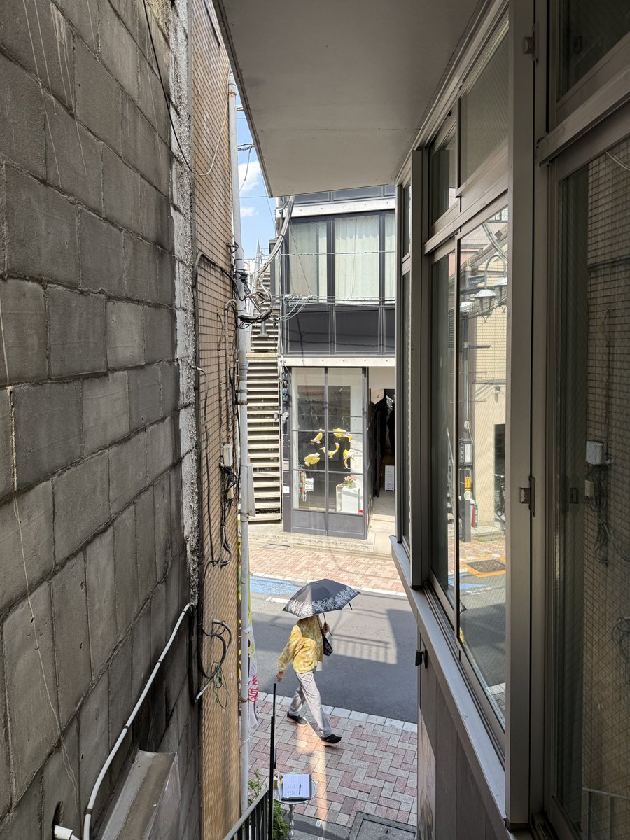 remgoto's tweet photo. 寳神尚史さんが主宰する日吉坂事務所が完成させた西荻窪の商業ビル「KITAYON KADO」の内覧会に訪問した。

内覧会とはいえ、既に各階のテナントさんが入居されており、稼働している状況で拝見できたのも良かった。

まずもって、この建築で伝えておきたいのは、設計だけでなく、日吉坂事務所が事業主であるということ、、、、！
事業計画を立て、土地を手に入れて、設計して貸すという一連を建築家が行なっているのである。これは、本当にすごいなと思う。

この「KITAYON KADO」の向かいには、2017年に同じく日吉坂事務所が完成させた「KITAYON」という商業ビル（賃貸住戸も内包）があり、こちらも同じく事業主でもある。
つまり、日吉坂事務所による二つの建築が向かい合って建っている。

余談なのだけど、この一棟めの「KITAYON」を建築雑誌で見たときに、一行だけで小さく「設計者が事業主でもある」というニュアンスの記述があり、当時大きな衝撃を受けたことは今でも憶えている。
建築家が設計の前後に関わったり、設計と異なるビジネスを複合して行うということが、現在では普及しつつあるが、それを先駆的に行なっていたのが寳神さんなのだ。

今日も寳神さんとそのエピソードを振り返るような話をさせて貰ったのだけれど、当時は、専門誌の誌面上で事業主でもあることを公表することに、少なからぬ躊躇もあったとのこと。建築家は形や空間をつくる専門家であるという感覚が今よりも強い時代だったのだろうと思う。これは、時代の感覚の記録としても意味のあるエピソードのように思う。

話を本建築に戻そう。
「KITAYON KADO」は鉄骨造で、建築面積約40m2の小さな商業ビルであり、一階にクッキーの販売店舗、二階にカフェを併設したギャラリー、三階に植物の販売も行うギャラリーが入居している。

上階には、隣地側に設けられた階段でアプローチするのだけれど、この階段空間が実に豊かで驚く。隣地建物の外壁の質感が生かされていたり、奥側の敷地への視線の抜けが作られていたりして、ワクワクした高揚感が生み出されている。

そう考えて、「KITAYON」を含むこれまでに経験した日吉坂事務所の建築を振り返ると、どの作品もこのような細長い空間が特徴であったことに気づく。建築スケールで言えばスリット、都市スケールで言えば路地と言える細長い空間が、どの建築にも備わっていて、周辺環境と呼応していてポジティブに雑多さを取り込んで、何というか「東京的な空間」を生み出していると思った。

3階のギャラリーに設けられたスリット側のバルコニーも、その感覚の流れにある空間で外に出たときに、ワクワク感を感じた、、、！恐らく、ここに寳神さんの都市観、東京観が、凝縮しているのでないかと思った。（こんど聞いてみよう）

また、単体の建築だけではなく、日吉坂事務所による商業ビルが二つ並んで建っているということについて感じたことも書いてみたいと思う。

ます、敷地は、西荻窪の駅から少し歩いたところで、商業店舗が沢山あるエリアから住宅街に切り替わる境目のような場所にある。

寳神さんと話をしていて、向かい側の土地を購入するのではなく、もう少し離れた土地を買ってビルを建てるという選択肢もあったのだという。
僕自身も内覧会を訪問する前に、あえて距離の離れた位置に建てることで、広範囲の関係性を生み出せるのという考え方もあるのではないかと思ったりした。

実際に2棟が建ち並んでいる様子を見て、また、先に書いた敷地の条件を見て思ったのは、寳神さんが、この場所に建築を並べることで、点を「群」にして、単なる店舗ではなく、街の目的地にしようとしたのだということが分かった。
商店街の歩いた先に、目的地を作ることで、駅と商店街の間の活性化が誘発されることを狙っているのではないかと思った。

僕は2000年前後に京都市で学生生活を送ったのだけれど、都市の中心地から離れた、北山という畑もある牧歌的なエリアに、当時のファッションの最先端のセレクトショップだった「ビームス」が存在していたことを思い出した。
駅から少し歩く離れた場所に会ったのだけれど、その求心的な店に行くためにみんな歩いていたし、その状況を活かすために間に様々なファッション店舗が建ち並ぶ状況がそこにはあった。この2棟の建築を見ていて、その光景が甦った、、、！

寳神さんが常々言っている、「建築家が事業主になるからこそ、事業性に振り切らない選択肢が取れる」という思想から生まれた街に貢献する商業ビル。そして、更にそれらが郡となっていくことで、その思想や選択肢が強化され、街に伝播していく。そのような姿が目に見えるようだった、、、！

また、一棟めの「KITAYON」の隣地の土地も取得済みであり、開発の予定も進めているのだという、、、！

寳神さん、事務所の皆さん、入居されている皆さん、ご竣工おめでとうございます！