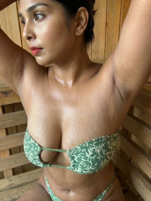 dj_rihya11's tweet photo. With both arms raised high, she confidently showcases the smooth, natural beauty of her armpits—soft skin glowing with a light sheen of sweat under the warm light. The green leafy bikini top hugs her full curves beautifully, drawing the eye upward to those elegantly exposed underarms that add an intimate, vulnerable yet powerful touch to her pose. Her side profile, with that intense gaze and slightly parted lips, radiates quiet confidence and raw sensuality, turning a simple stretch into something undeniably alluring and bold.