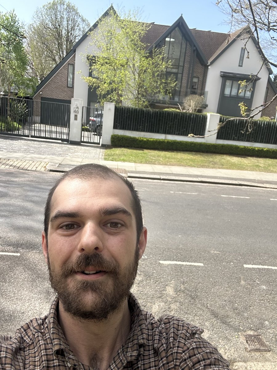 rockwellmemes's tweet photo. We see a man in the middle of the road, posing in front of a house, but the house is gated implying it isn’t his. Then why does he smile in awe? Maybe it’s because despite not achieving his dream for the first time in his life he knows that it’s achievable, for it is right there in front of him.